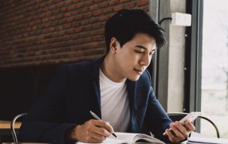 young asian man taking notes and looking at his phone
